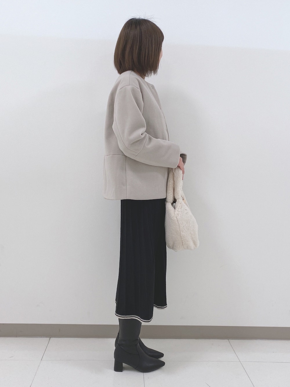 ベージュ系のノーカラーコート、ブラック系のワンピース、ブラック系のブーツを着用したレディースの冬コーディネートの2枚目の写真