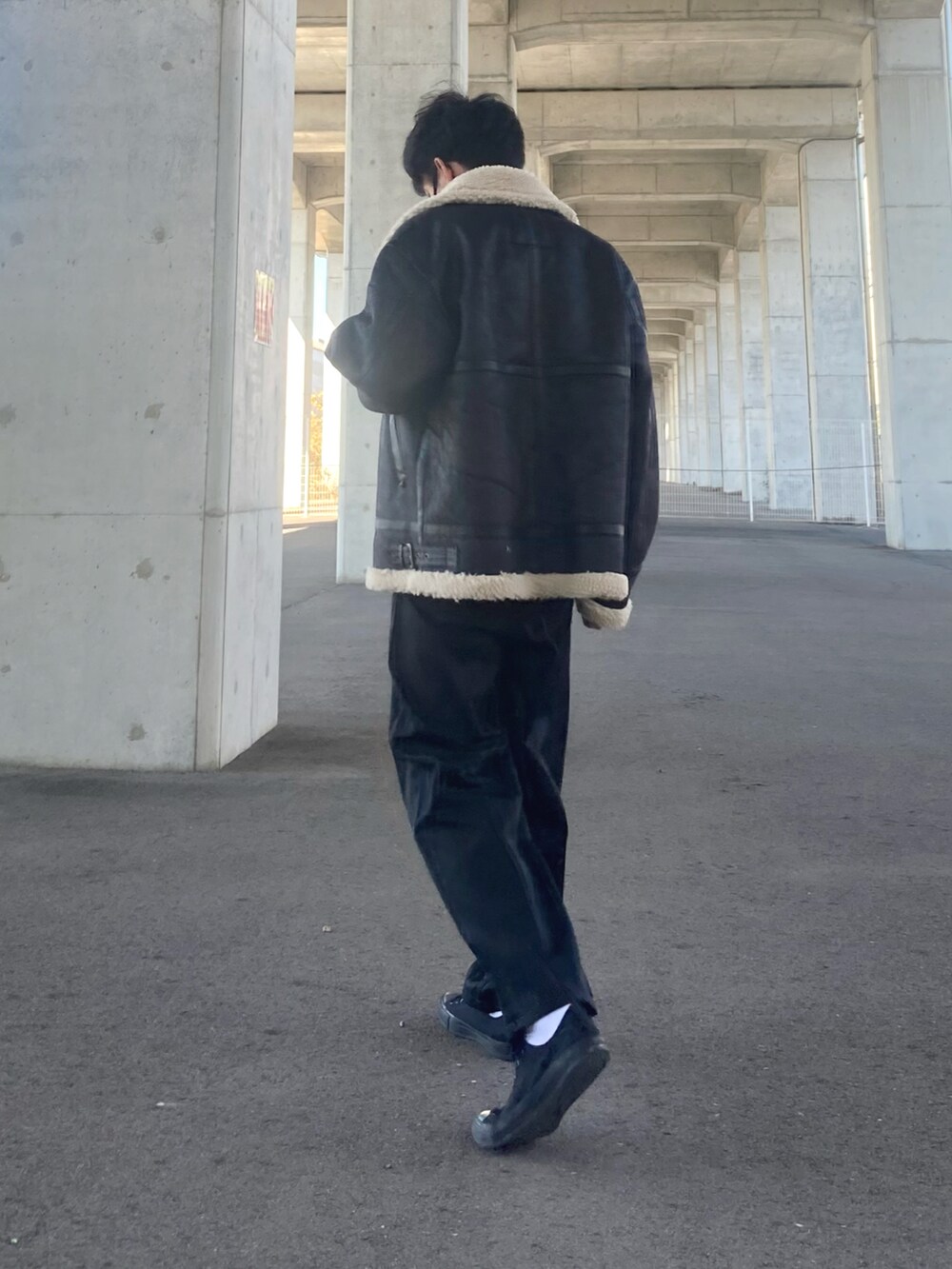 ブラック系のムートンコート、ブラック系のスラックス、ブラック系のスニーカーを着用したメンズの秋コーディネートの3枚目の写真