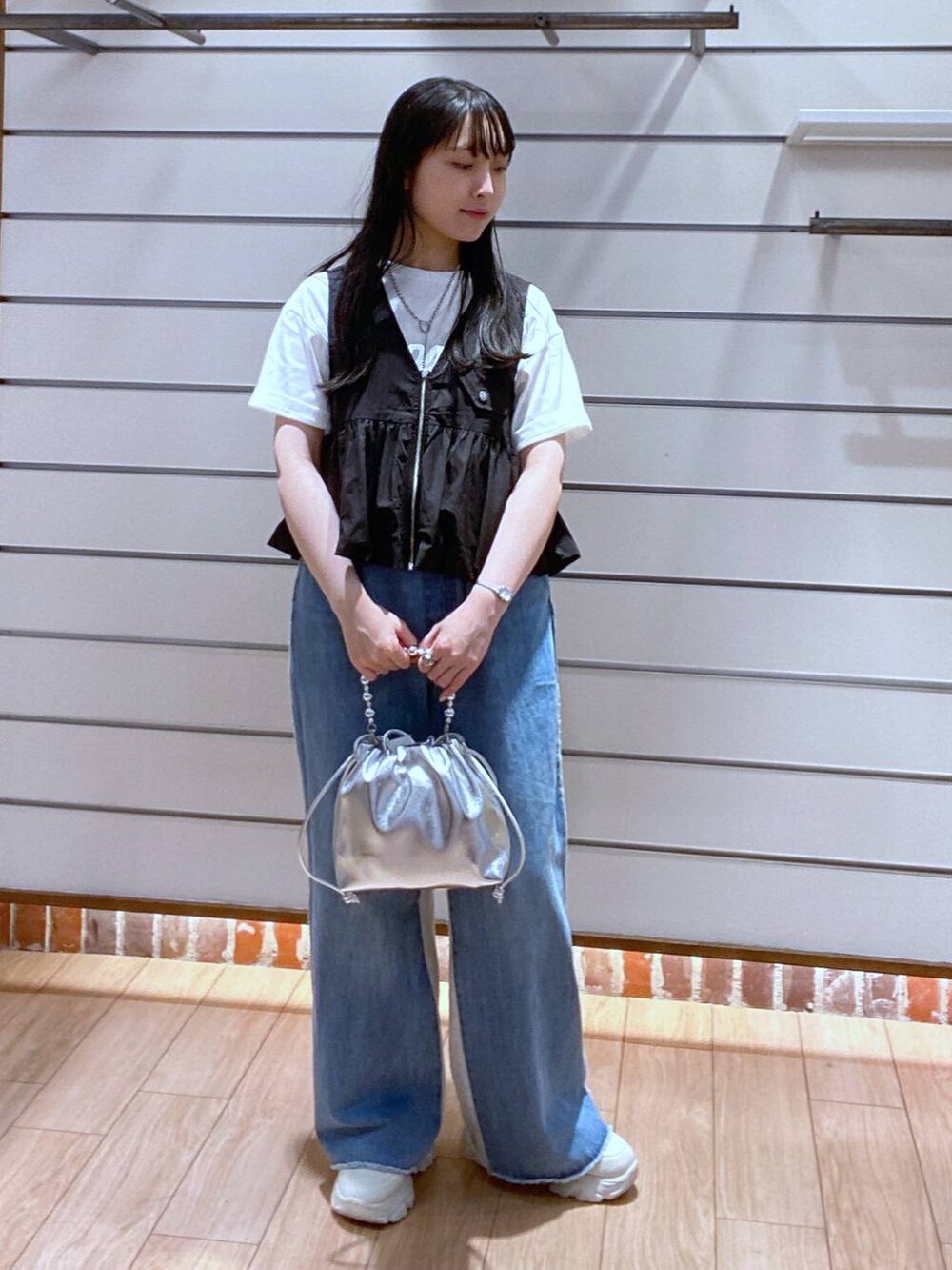 ブルー系のデニムパンツ、ブラック系のベスト、シルバー系のショルダーバッグを着用したレディースの夏コーディネートの2枚目の写真