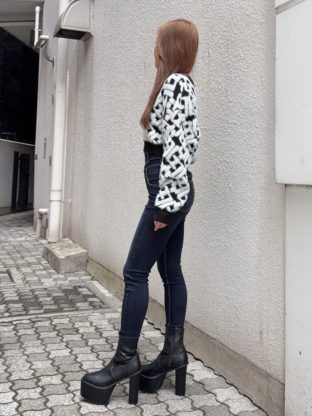 ブラック系のニット/セーター、ブルー系のデニムパンツ、ブラック系のブーツを着用したレディースの秋コーディネートの2枚目の写真