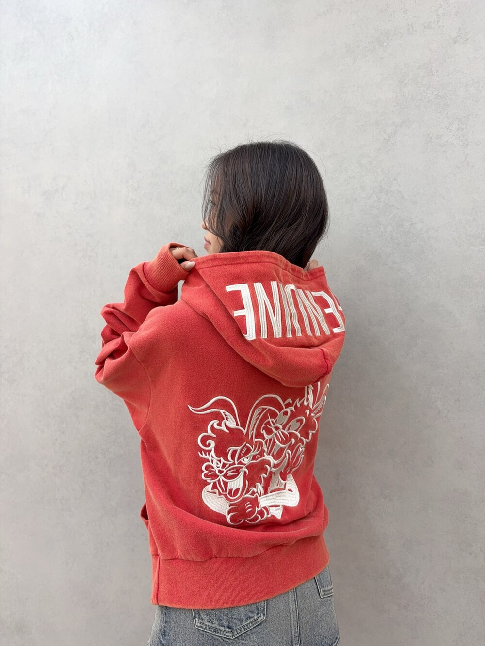 レッド系のパーカー、ブルー系のデニムスカート、ブラック系のブーツを着用したレディースの秋コーディネートの4枚目の写真