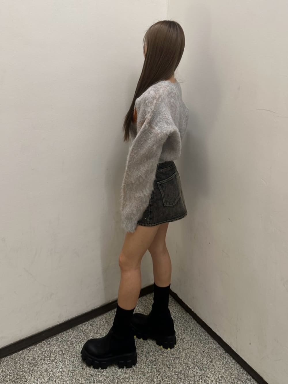 グレー系のニット/セーター、ブルー系のデニムスカート、ブラック系のブーツを着用したレディースの冬コーディネートの2枚目の写真