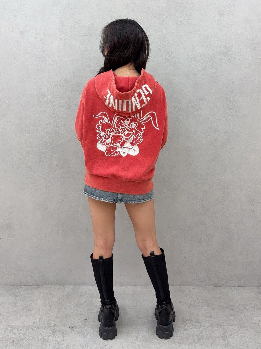 レッド系のパーカー、ブルー系のデニムスカート、ブラック系のブーツを着用したレディースの秋コーディネートの3枚目の写真