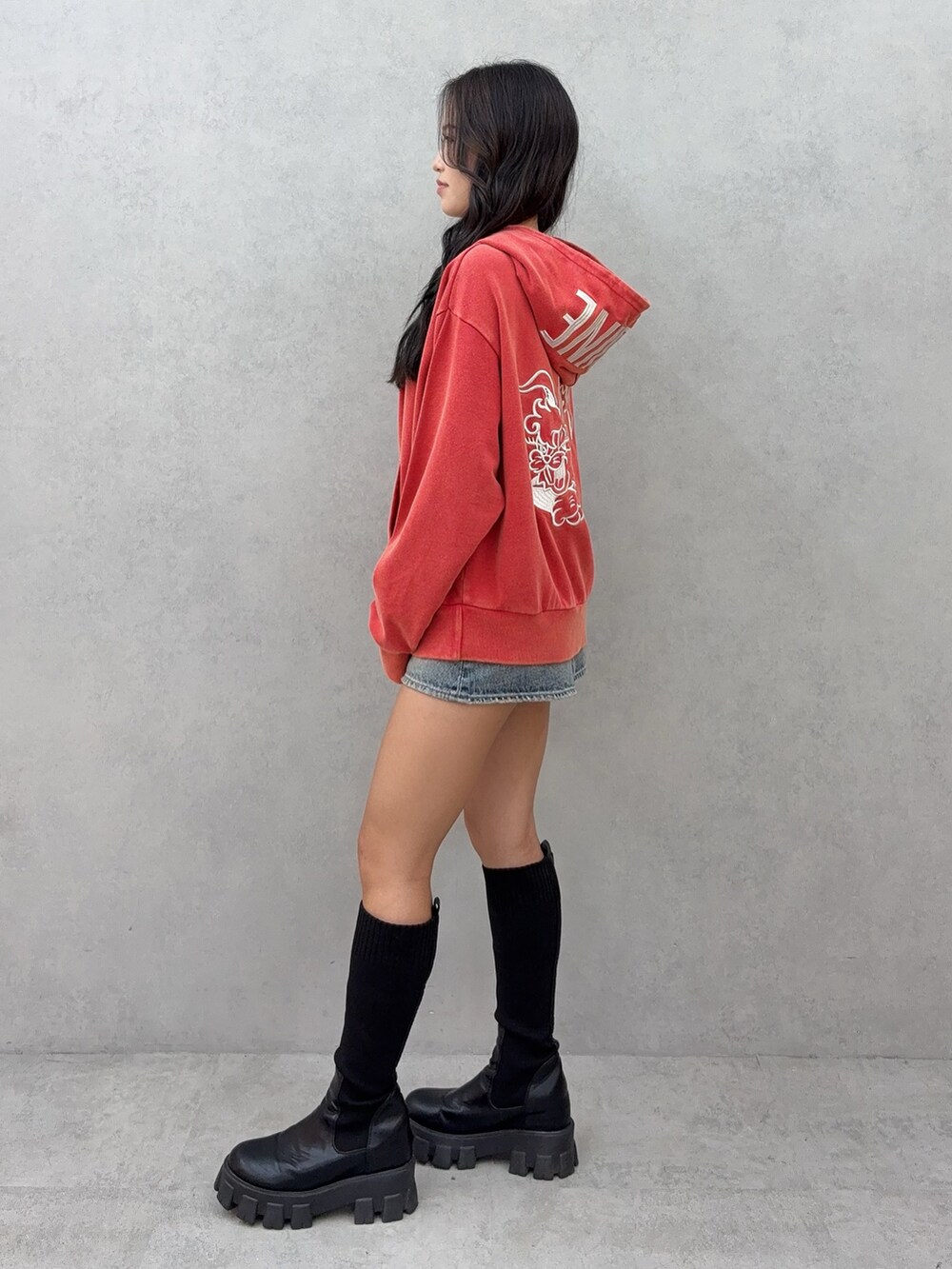 レッド系のパーカー、ブルー系のデニムスカート、ブラック系のブーツを着用したレディースの秋コーディネートの2枚目の写真