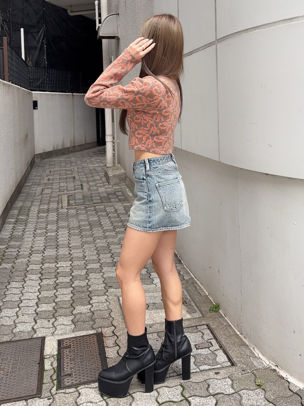 オレンジ系のニット/セーター、ブルー系のデニムスカート、ブラック系のブーツを着用したレディースの秋コーディネートの2枚目の写真