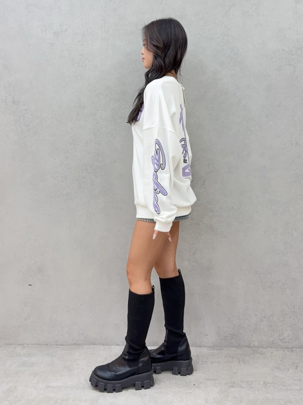 ホワイト系のスウェット、ブルー系のデニムスカート、ブラック系のブーツを着用したレディースの秋コーディネートの2枚目の写真