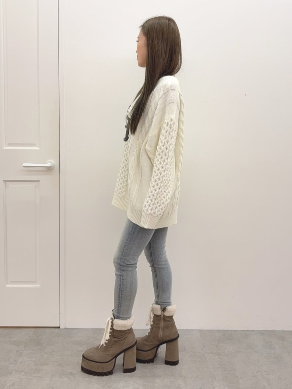 ブルー系のデニムパンツ、ベージュ系のブーツ、ホワイト系のニット/セーターを着用したレディースの秋コーディネートの2枚目の写真