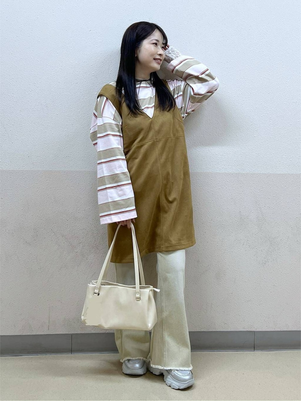 ホワイト系のハンドバッグ、イエロー系のワンピース、ベージュ系のデニムパンツを着用したレディースの冬コーディネートの4枚目の写真