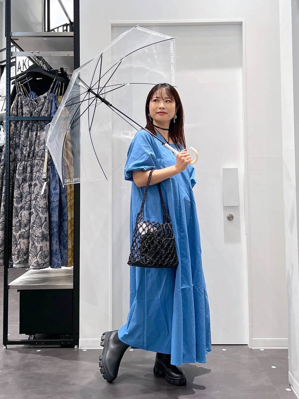 ブラック系のかごバッグ、ブラック系のレインシューズ、ブルー系のワンピースを着用したレディースの春コーディネートの3枚目の写真