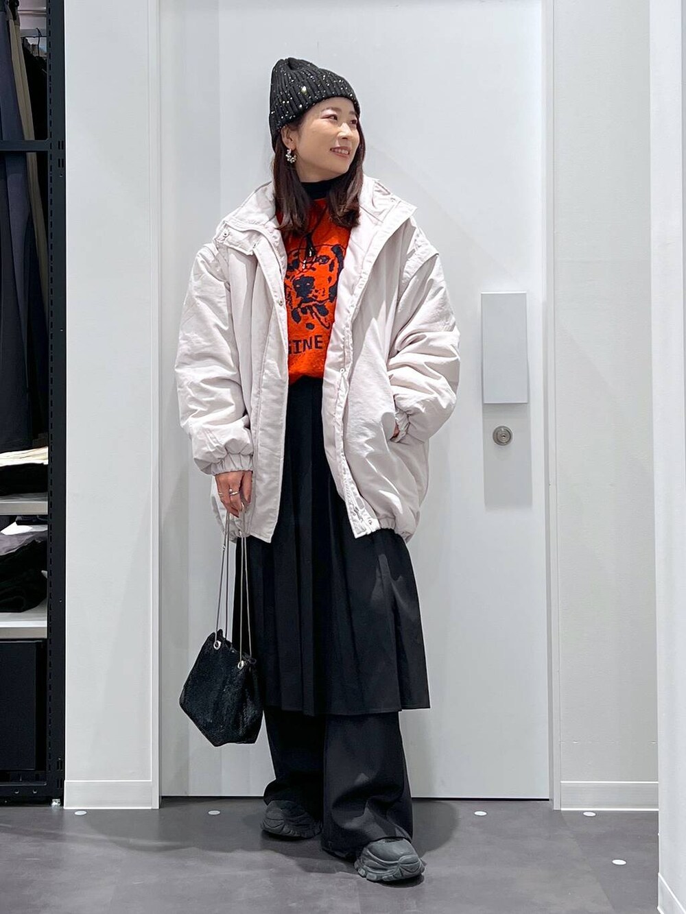 オレンジ系のニット/セーター、グレー系のその他アウター、ブラック系のブーツを着用したレディースの冬コーディネートの3枚目の写真