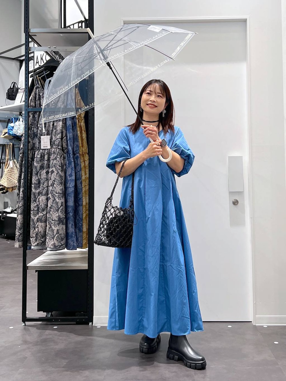 ブラック系のかごバッグ、ブラック系のレインシューズ、ブルー系のワンピースを着用したレディースの春コーディネートの2枚目の写真