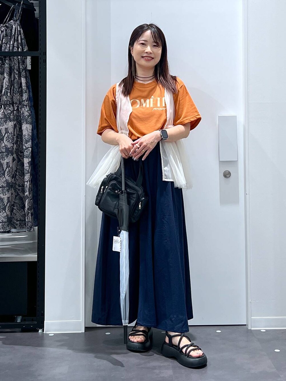 ブラック系のサンダル、オレンジ系のTシャツ/カットソー、ベージュ系のベストを着用したレディースの夏コーディネートの5枚目の写真