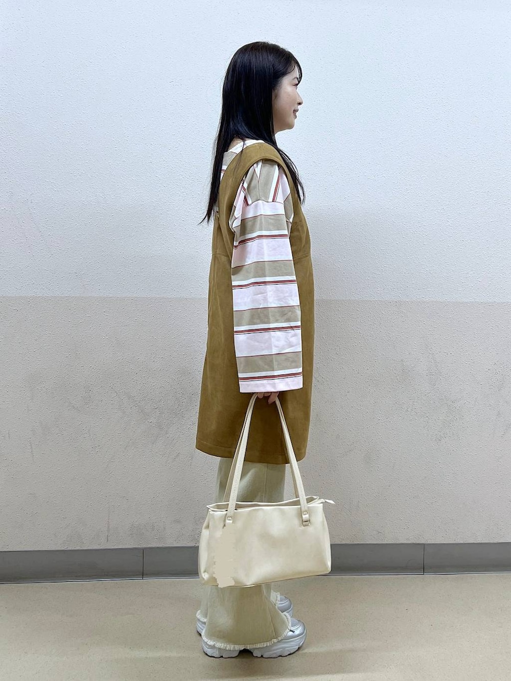 ホワイト系のハンドバッグ、イエロー系のワンピース、ベージュ系のデニムパンツを着用したレディースの冬コーディネートの2枚目の写真