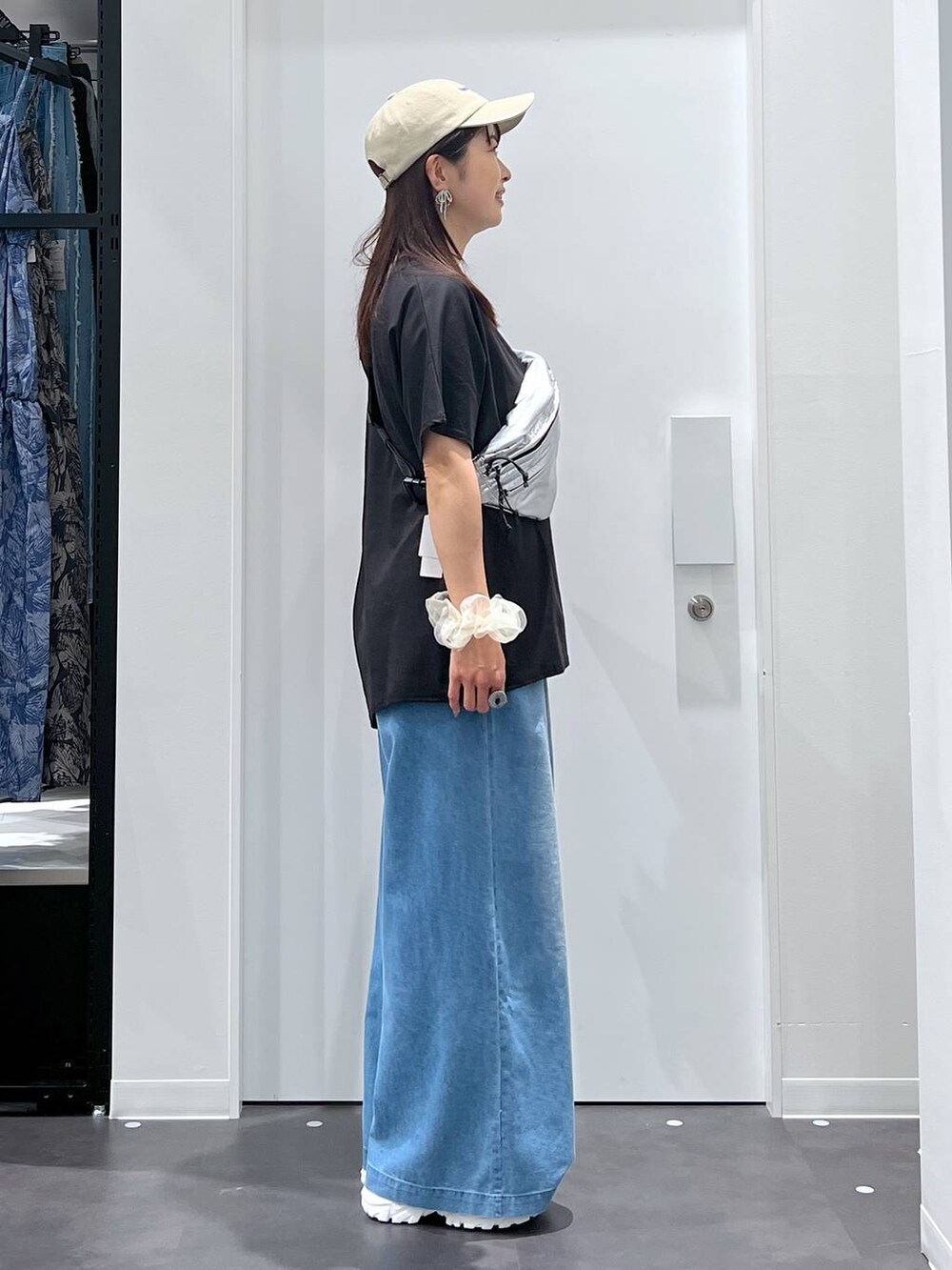 シルバー系のボディバッグ/ウエストポーチ、ホワイト系のスニーカー、ブルー系のデニムパンツを着用したレディースの夏コーディネートの2枚目の写真