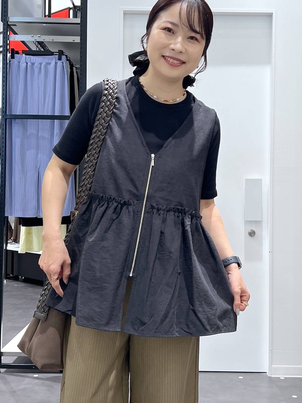 ブラウン系のショルダーバッグ、イエロー系のスラックス、ブラック系のベストを着用したレディースの夏コーディネートの4枚目の写真