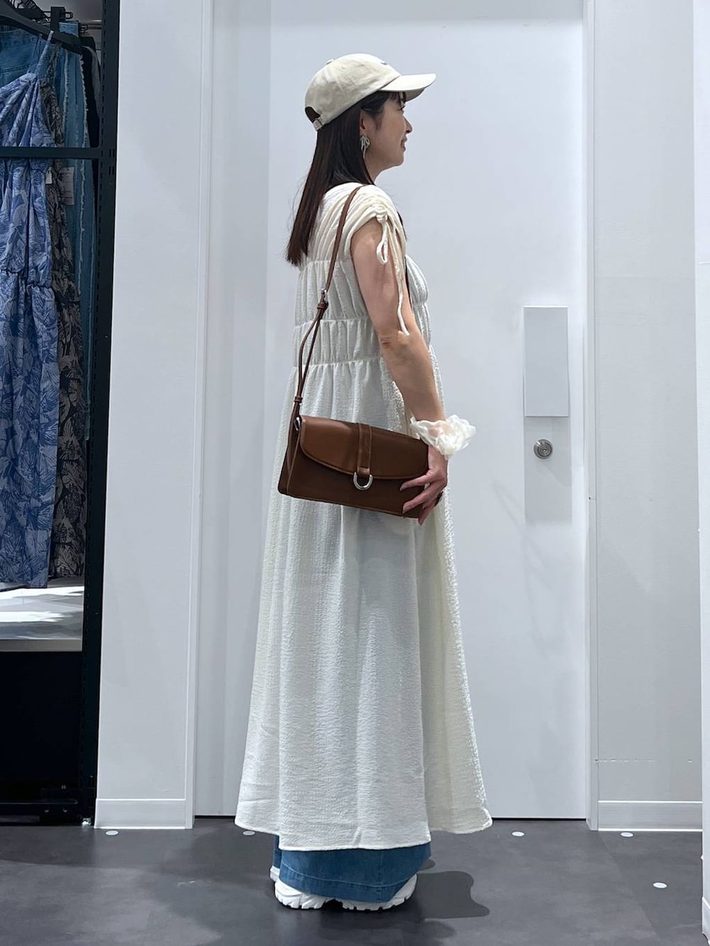 ホワイト系のスニーカー、ブラウン系のショルダーバッグ、ブルー系のデニムパンツを着用したレディースの夏コーディネートの2枚目の写真