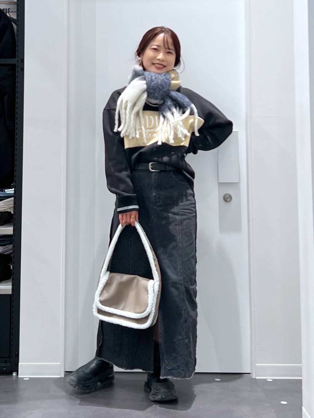 ブラック系のブーツ、ベージュ系のショルダーバッグ、ブラック系のデニムスカートを着用したレディースの冬コーディネートの2枚目の写真
