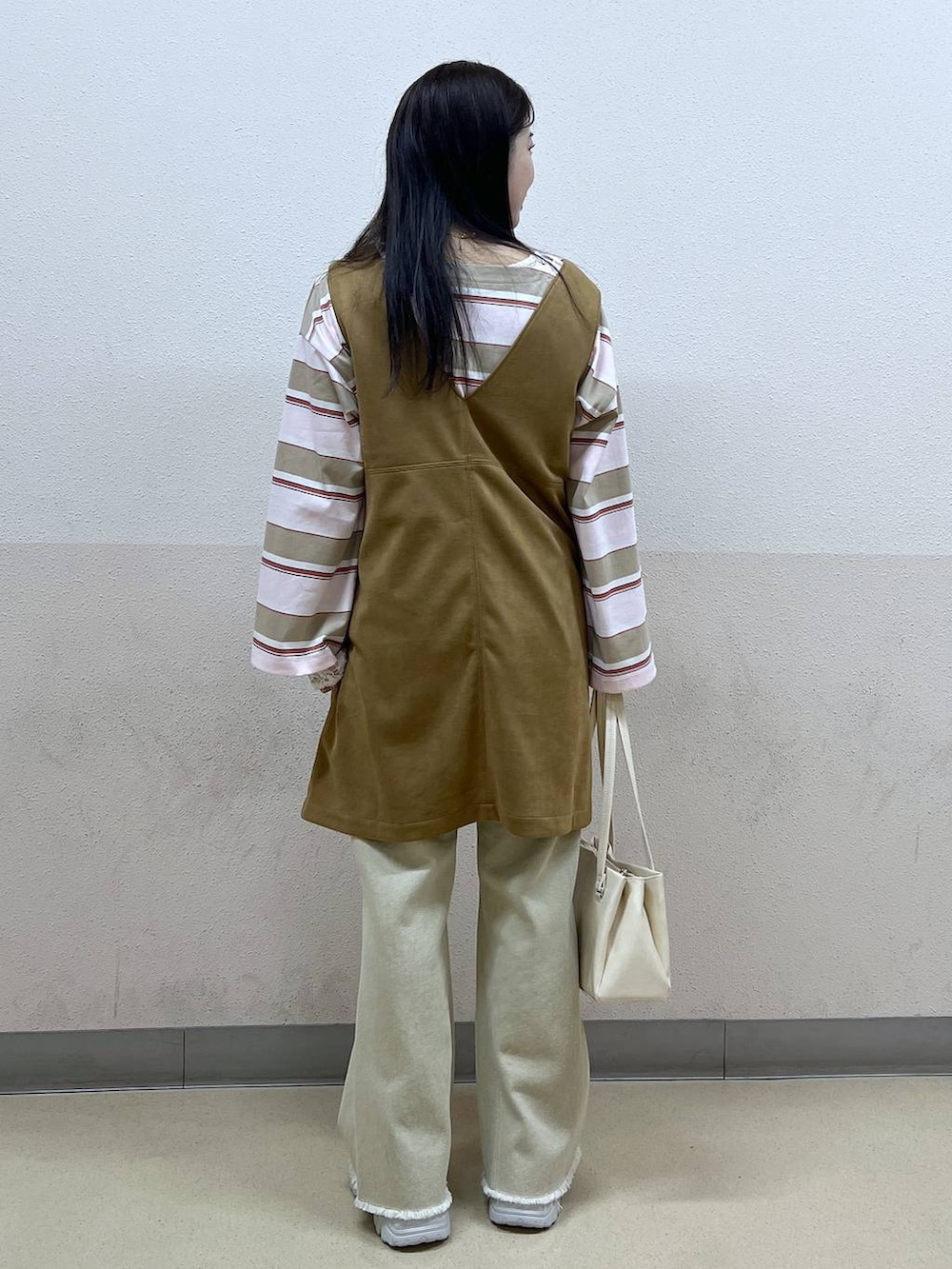 ホワイト系のハンドバッグ、イエロー系のワンピース、ベージュ系のデニムパンツを着用したレディースの冬コーディネートの3枚目の写真