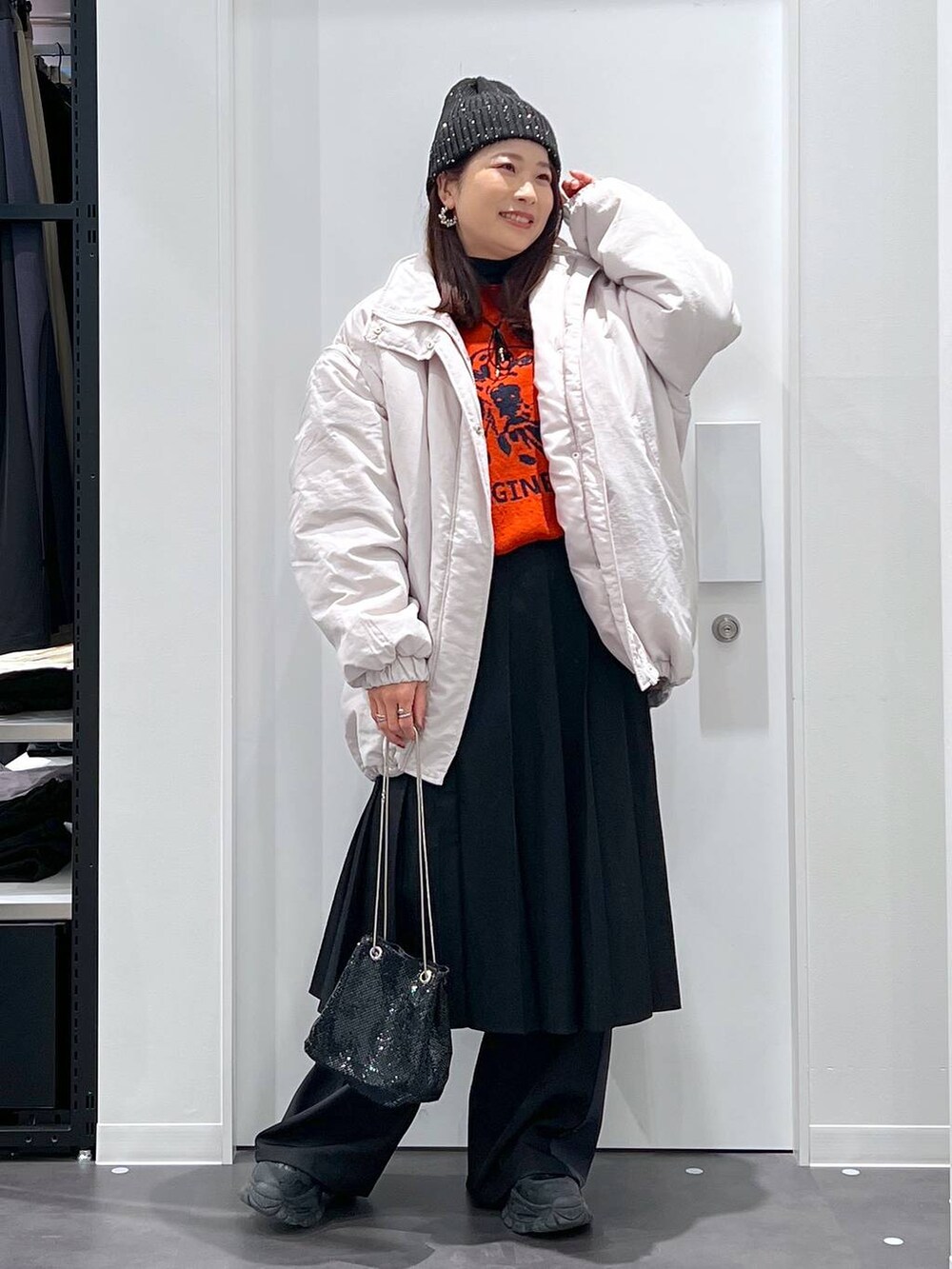 オレンジ系のニット/セーター、グレー系のその他アウター、ブラック系のブーツを着用したレディースの冬コーディネートの2枚目の写真