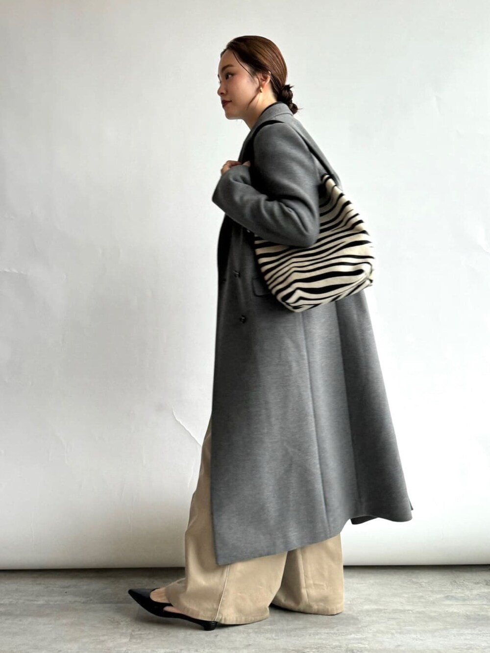 グレー系のチェスターコート、グレー系のカーディガン/ボレロ、ベージュ系のスラックスを着用したレディースの秋コーディネートの2枚目の写真