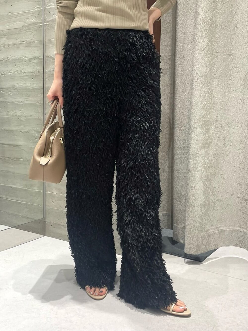 グリーン系のニット/セーター、ブラック系のスラックス、ベージュ系のショルダーバッグを着用したレディースの夏コーディネートの3枚目の写真