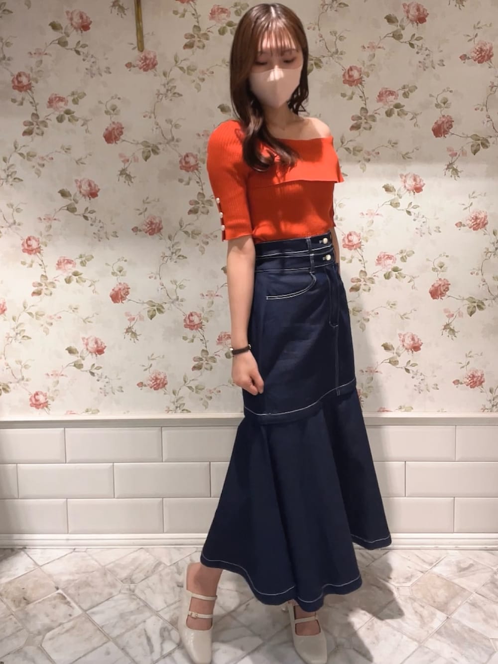 オレンジ系のニット/セーター、ブルー系のスカート、ホワイト系のパンプスを着用したレディースの春コーディネートの2枚目の写真