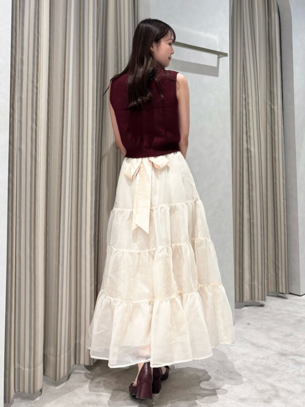 レッド系のニット/セーター、ベージュ系のスカート、ブラウン系のショルダーバッグを着用したレディースの秋コーディネートの4枚目の写真