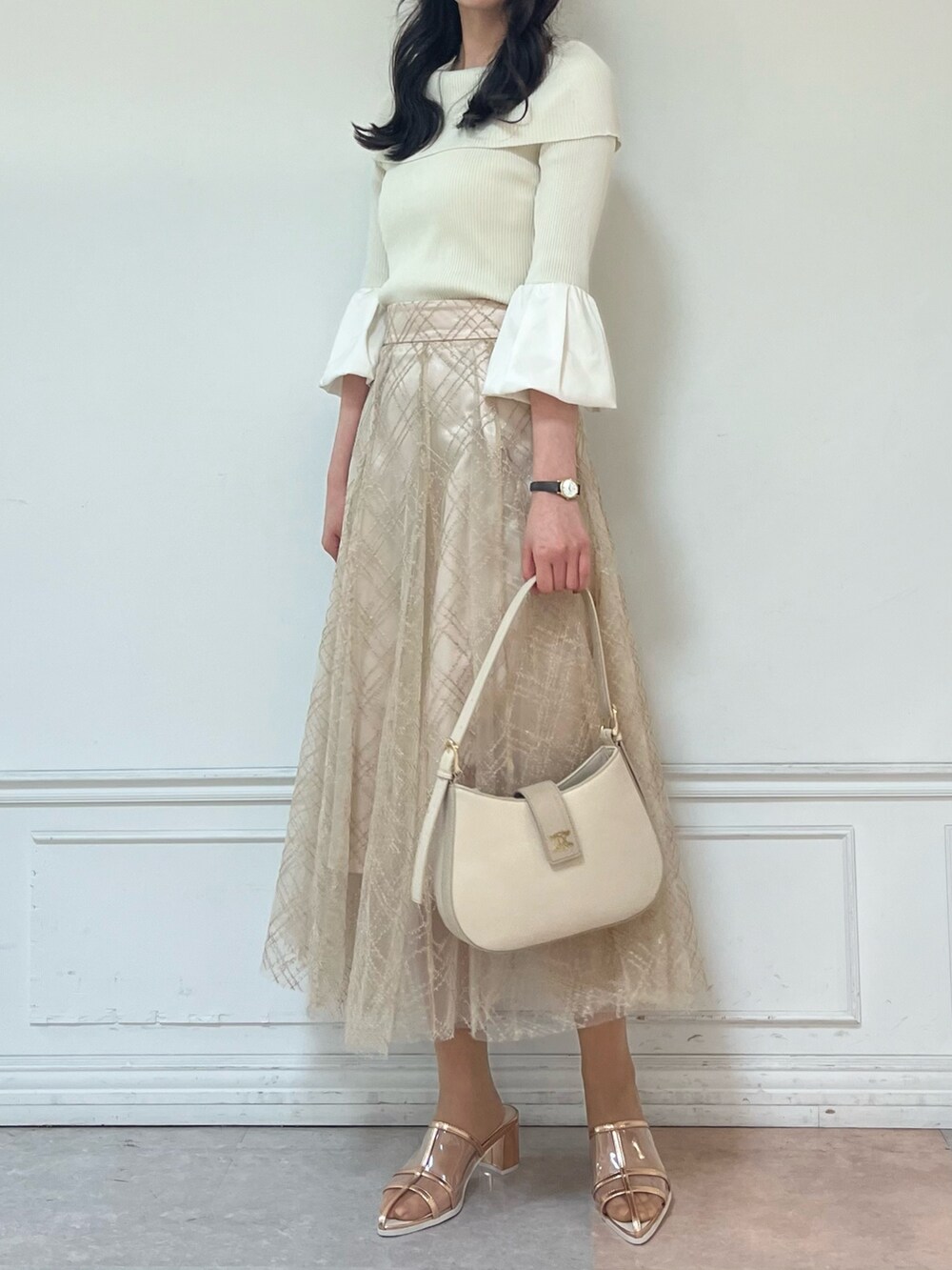 ベージュ系のスカート、ゴールド系のパンプス、ホワイト系のニット/セーターを着用したレディースの春コーディネートの2枚目の写真