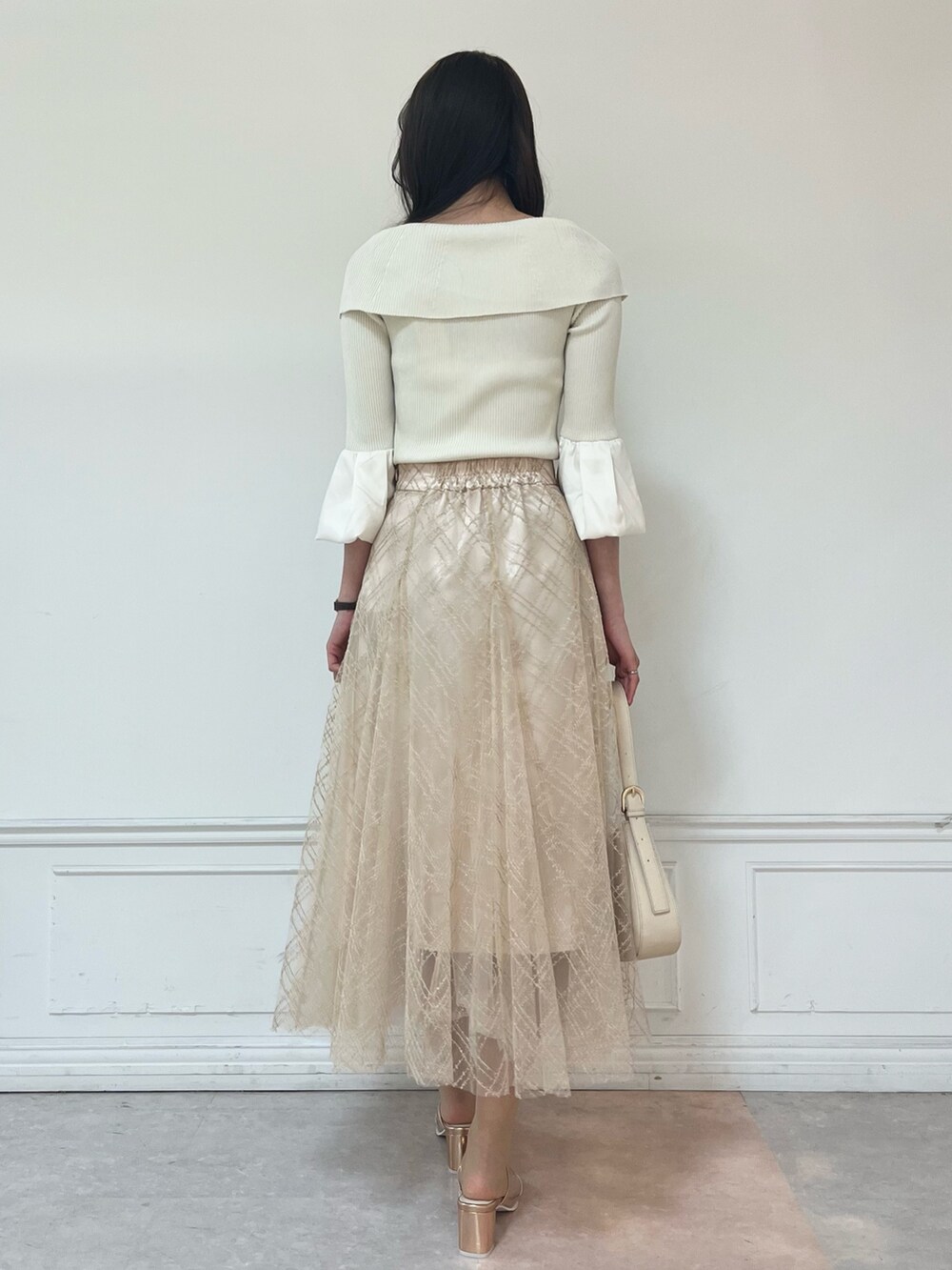 ベージュ系のスカート、ゴールド系のパンプス、ホワイト系のニット/セーターを着用したレディースの春コーディネートの3枚目の写真
