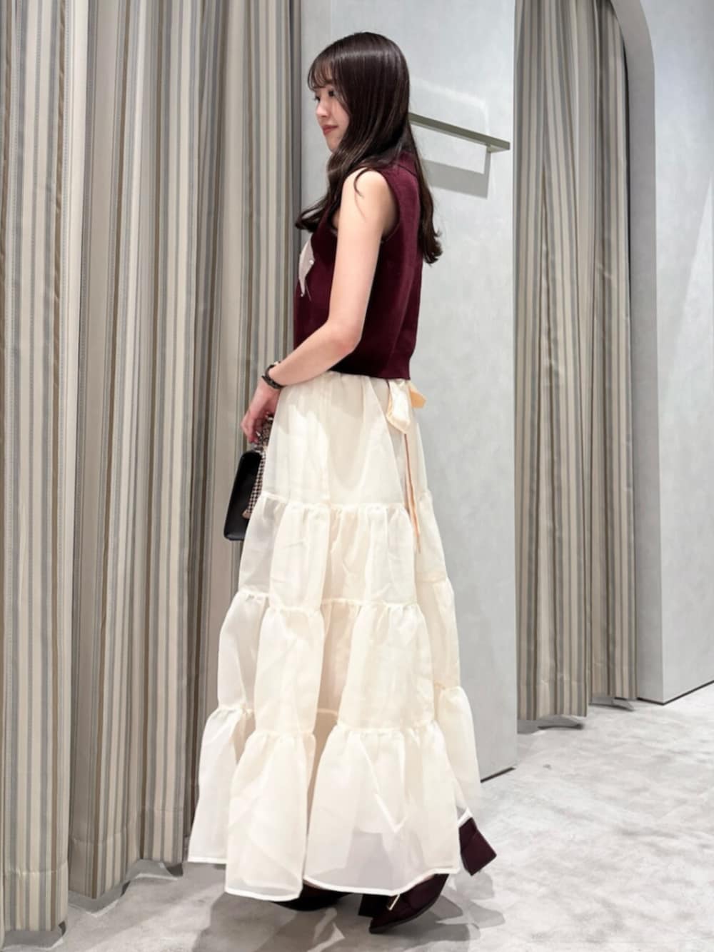 レッド系のニット/セーター、ベージュ系のスカート、ブラウン系のショルダーバッグを着用したレディースの秋コーディネートの3枚目の写真