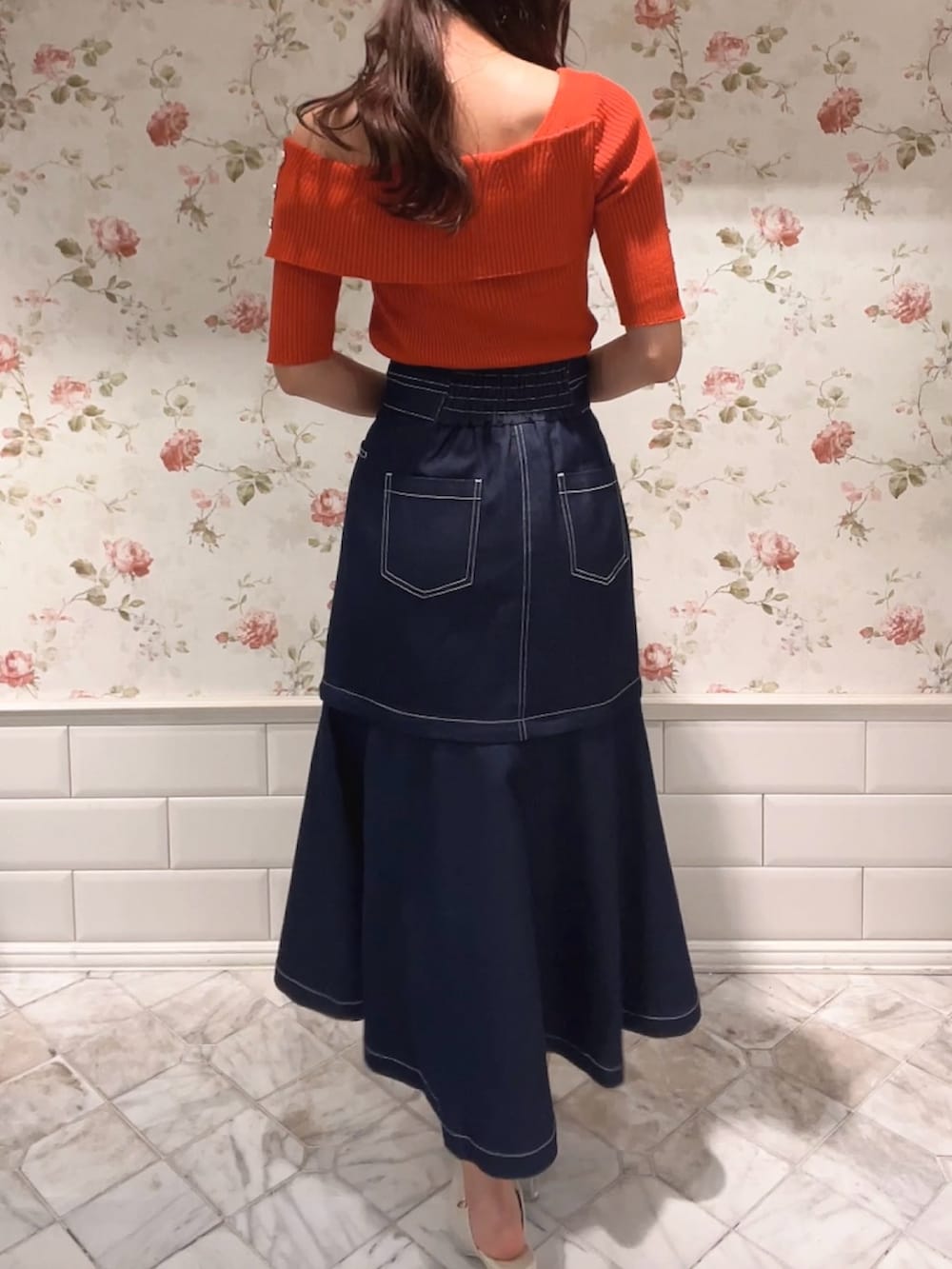 オレンジ系のニット/セーター、ブルー系のスカート、ホワイト系のパンプスを着用したレディースの春コーディネートの3枚目の写真