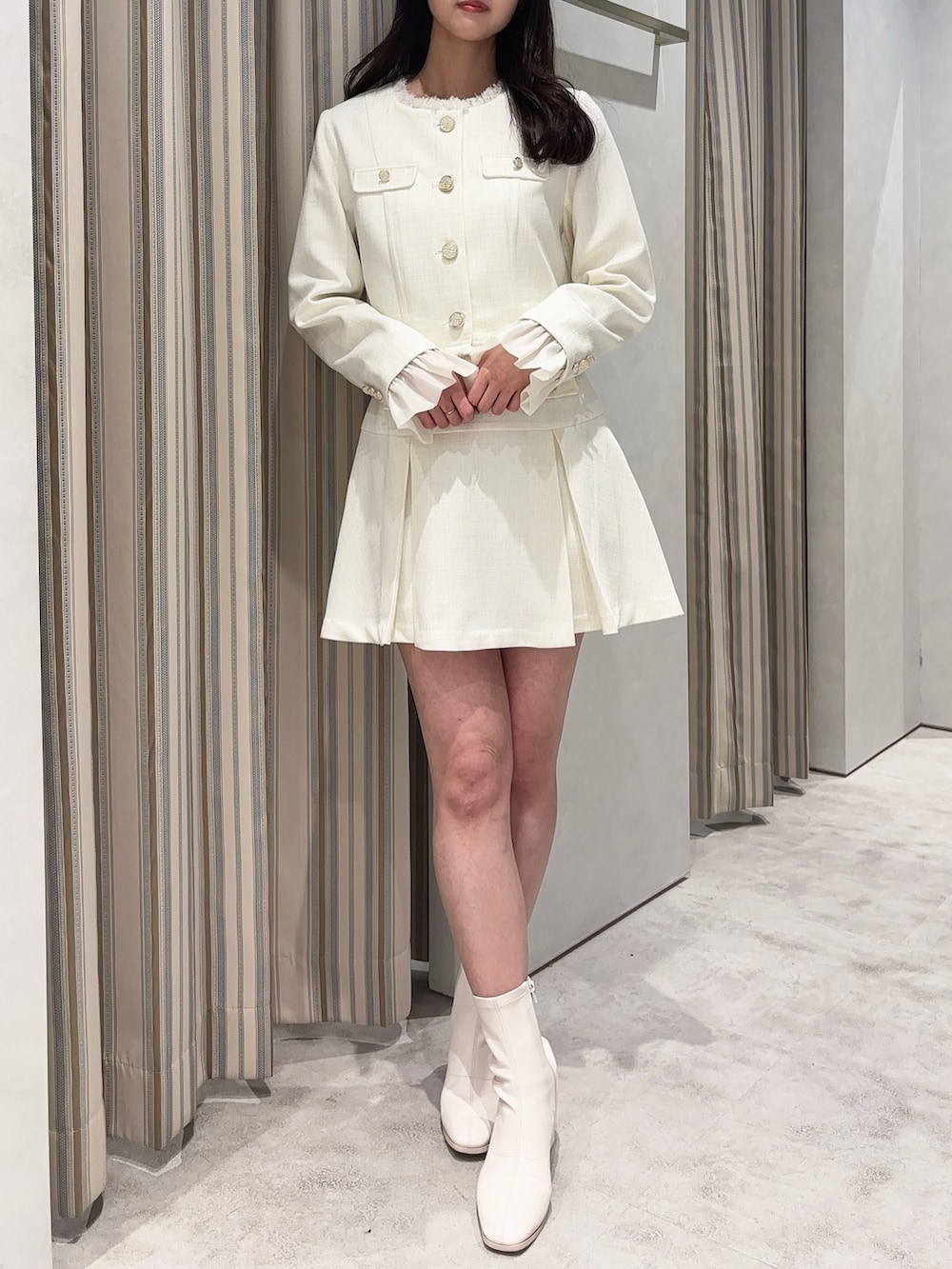 ホワイト系のノーカラージャケット、ホワイト系のスカート、ホワイト系のブーツを着用したレディースの春コーディネートの2枚目の写真