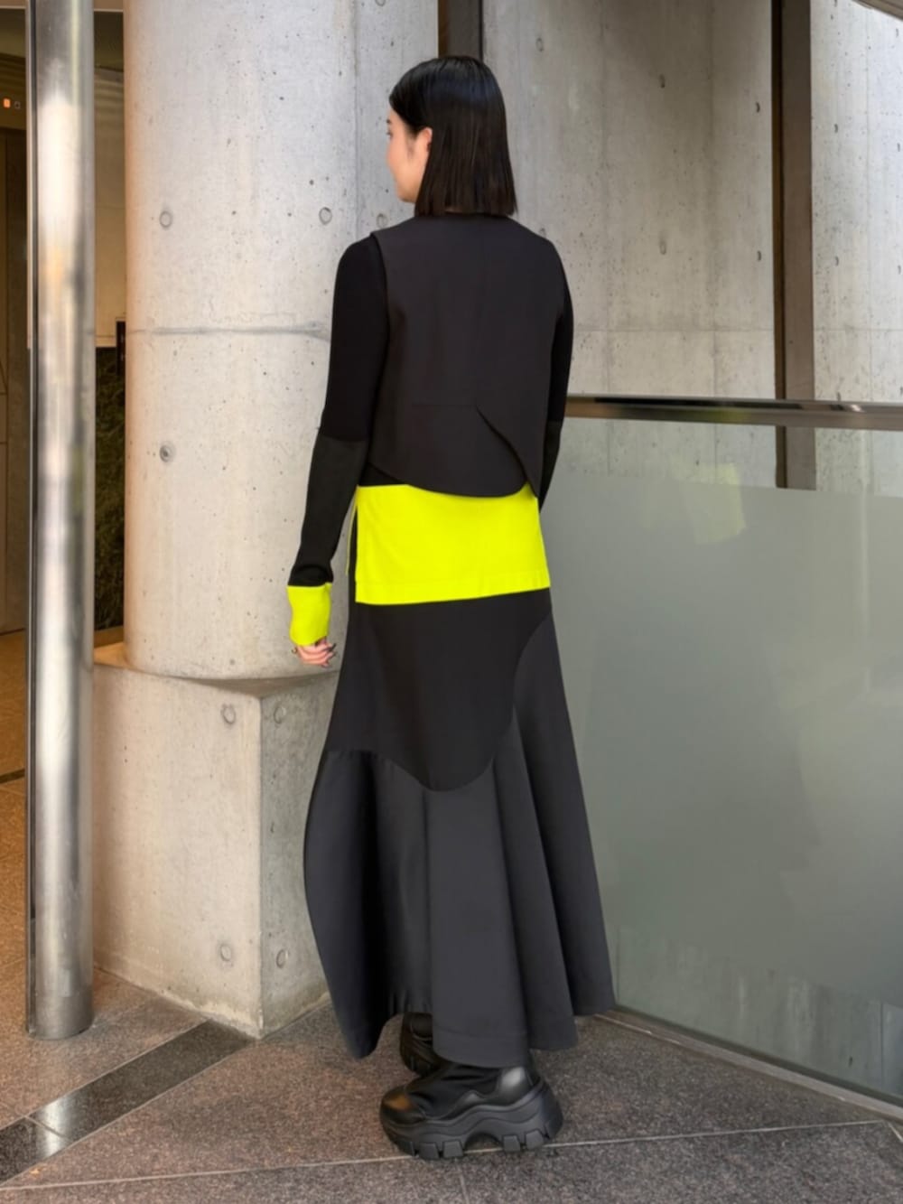 ブラック系のベスト、グリーン系のニット/セーター、ブラック系のスカートを着用したレディースの秋コーディネートの2枚目の写真