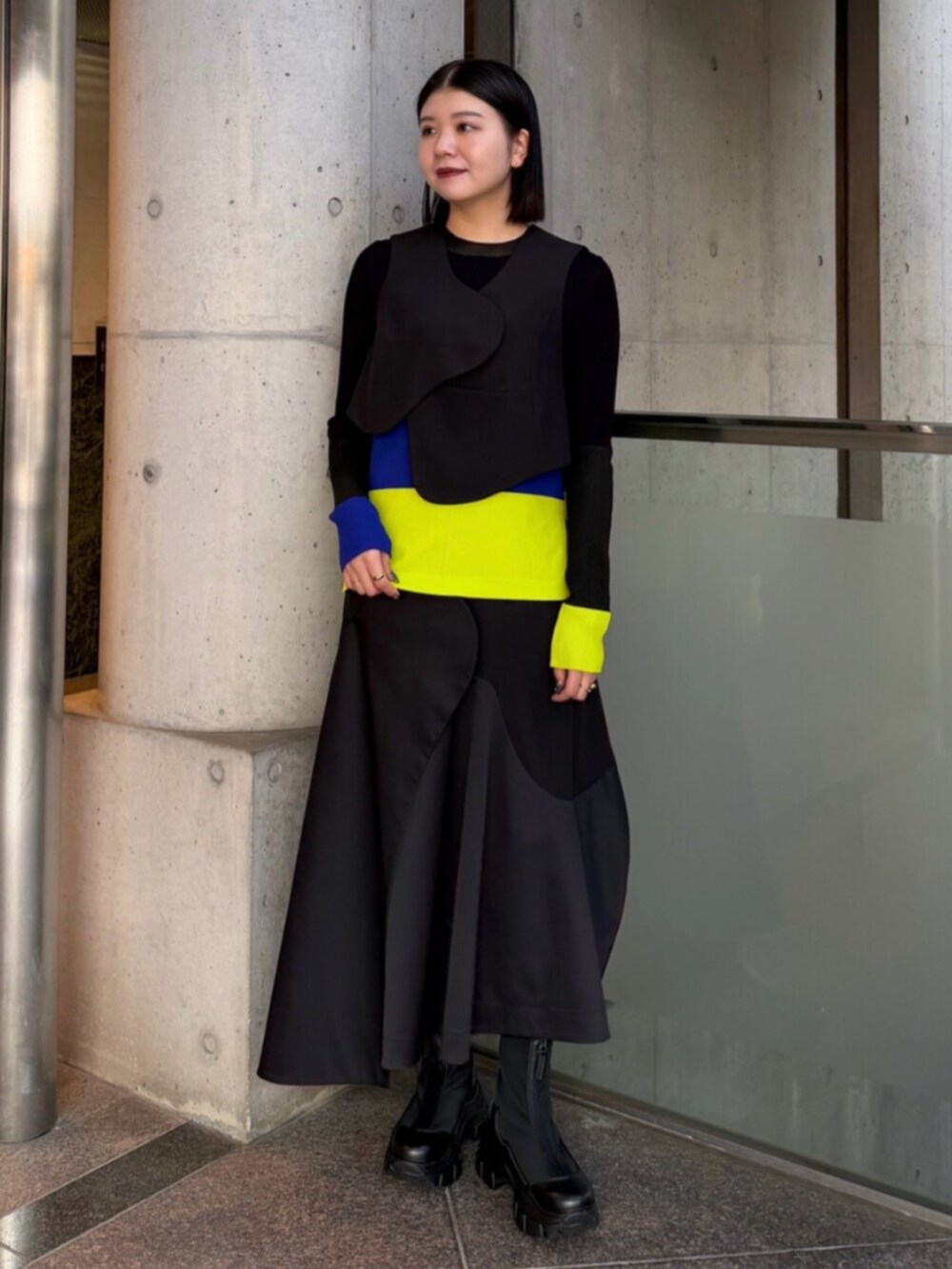 ブラック系のベスト、グリーン系のニット/セーター、ブラック系のスカートを着用したレディースの秋コーディネートの3枚目の写真