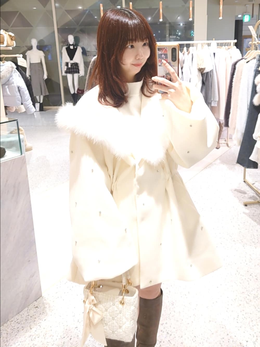 ホワイト系のノーカラーコート、ホワイト系のニット/セーター、ホワイト系のショルダーバッグを着用したレディースの冬コーディネートの2枚目の写真