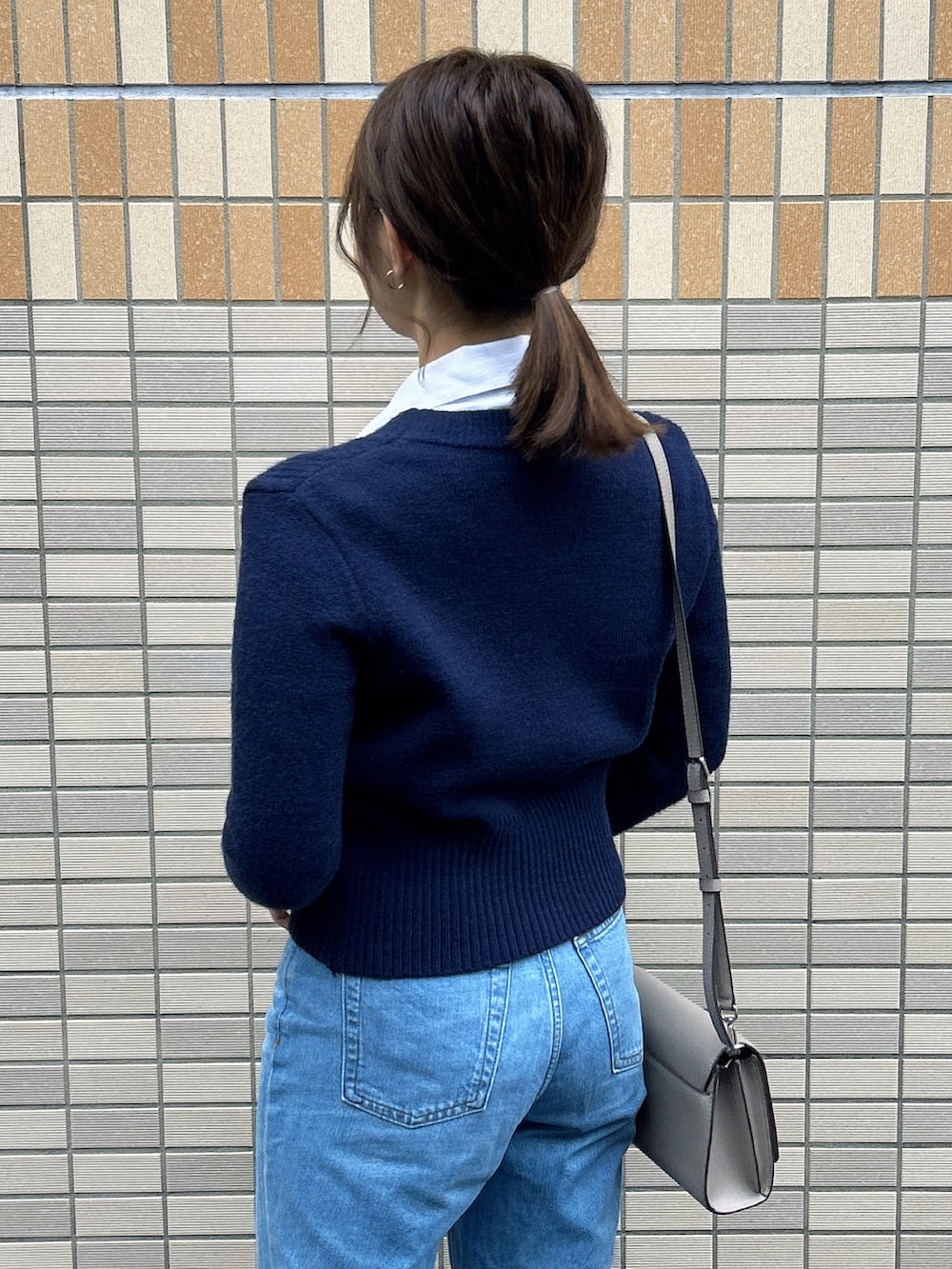 グレー系のショルダーバッグ、ブラック系のパンプス、ブルー系のデニムパンツを着用したレディースの秋コーディネートの3枚目の写真