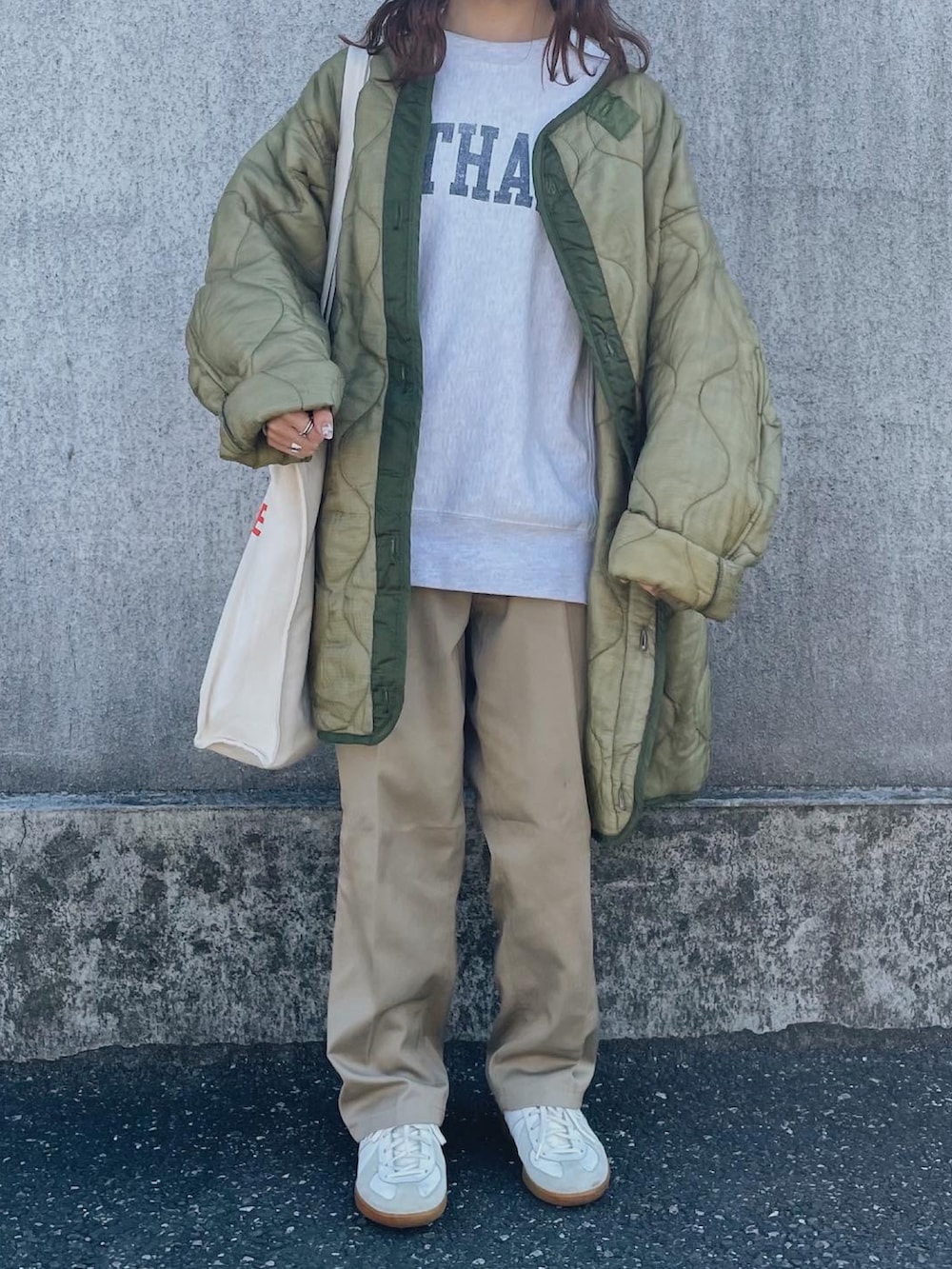 グレー系のスウェット、ベージュ系のトートバッグ、グリーン系のミリタリージャケットを着用したレディースの春コーディネートの2枚目の写真