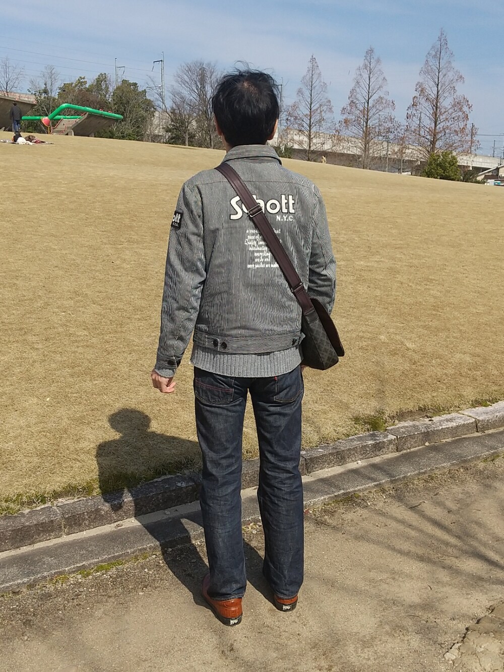 ブルー系のデニムジャケット、ブルー系のデニムパンツ、ブラウン系のスニーカーを着用したメンズの春コーディネートの2枚目の写真