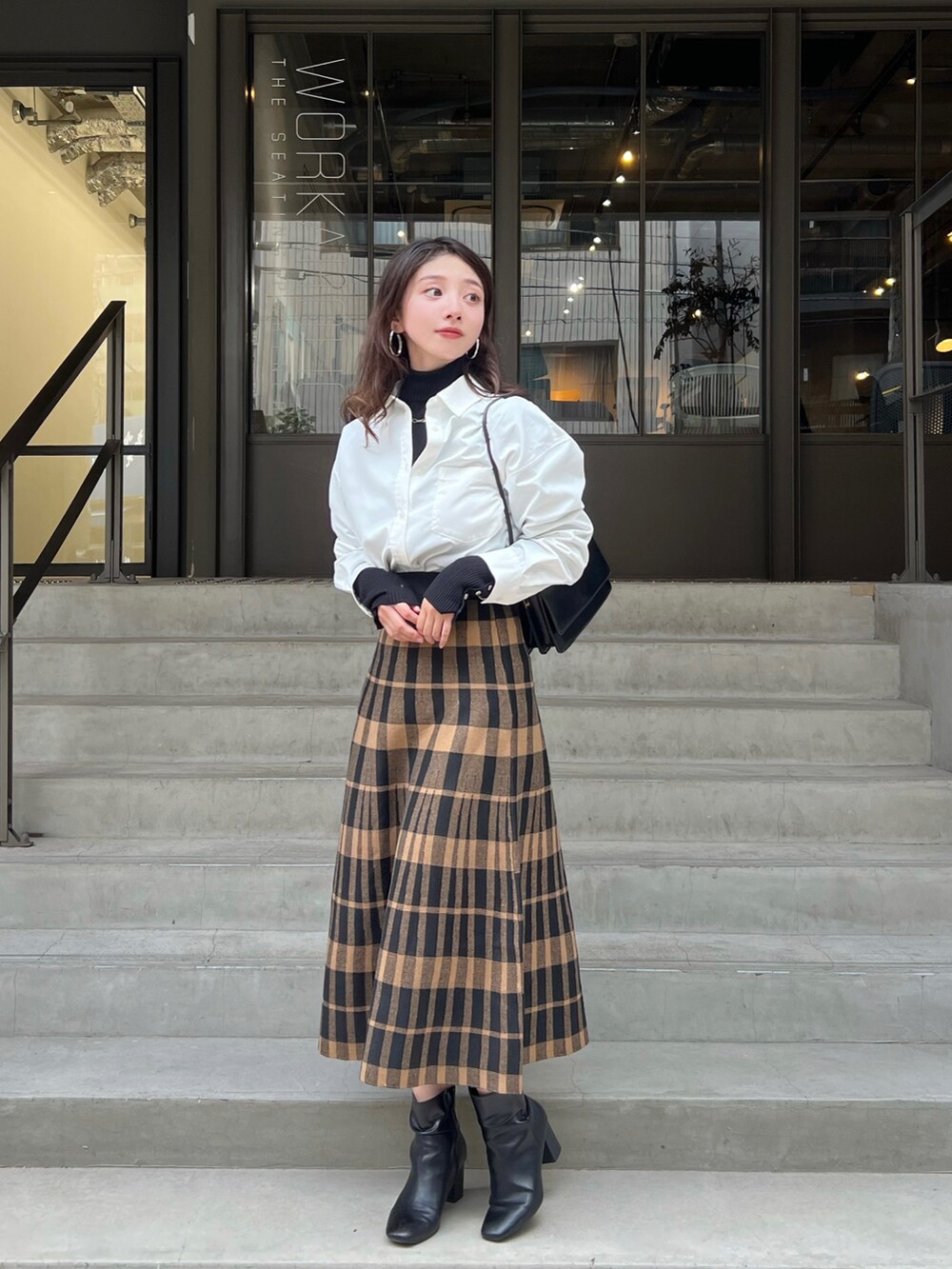 ベージュ系のスカート、ブラック系のニット/セーター、ブラック系のショルダーバッグを着用したレディースの秋コーディネートの2枚目の写真