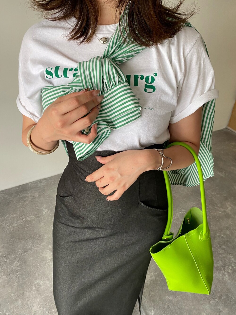 グリーン系のハンドバッグ、ホワイト系のサンダル、ホワイト系のTシャツ/カットソーを着用したレディースの夏コーディネートの2枚目の写真
