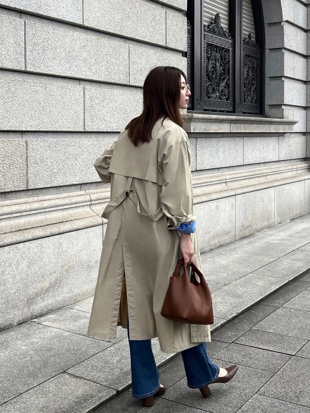 ブルー系のシャツ/ブラウス、ベージュ系のステンカラーコート、ブラウン系のハンドバッグを着用したレディースの春コーディネートの2枚目の写真