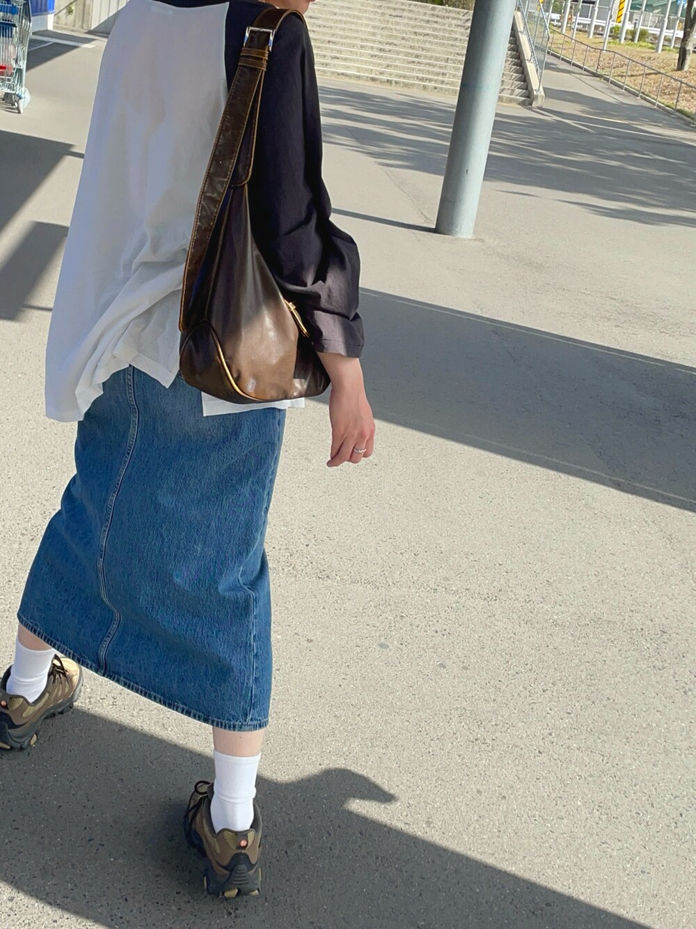 グレー系のトップス、ブルー系のデニムスカート、ブラウン系のシューズを着用したレディースの春コーディネートの2枚目の写真