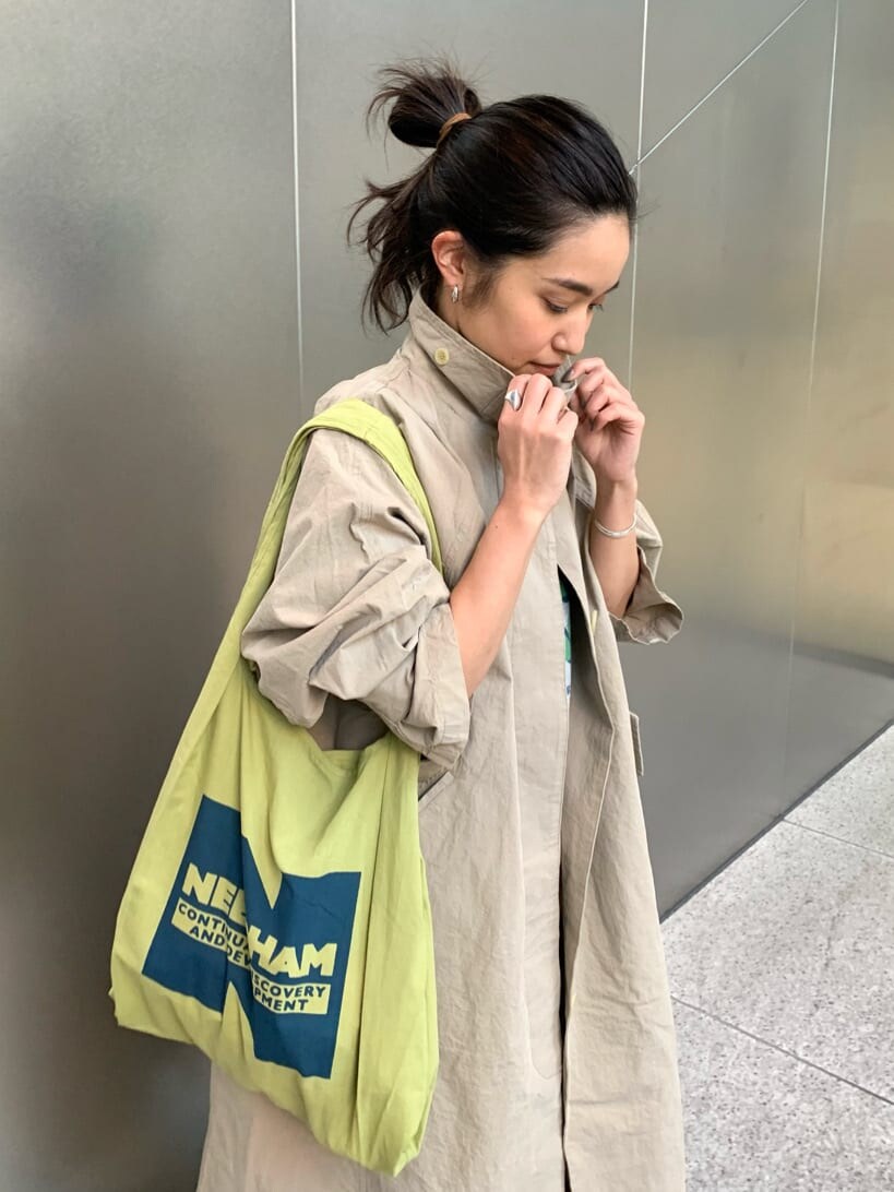 ベージュ系のステンカラーコート、ブラウン系のパンプス、グリーン系のエコバッグ/サブバッグを着用したレディースの冬コーディネートの2枚目の写真