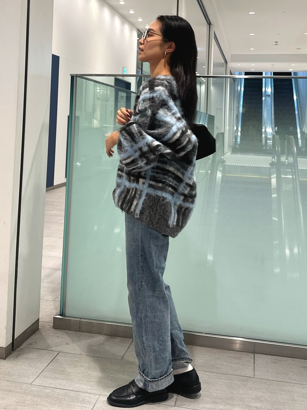 グレー系のニット/セーター、ブルー系のデニムパンツ、ブラック系のハンドバッグを着用したレディースの秋コーディネートの2枚目の写真