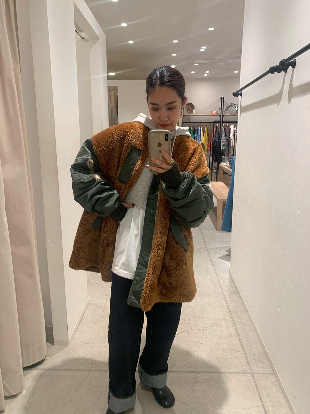 グリーン系のブルゾン、グレー系のパーカー、ブルー系のデニムパンツを着用したレディースの秋コーディネートの2枚目の写真