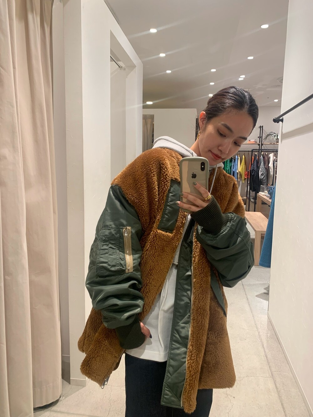 グリーン系のブルゾン、グレー系のパーカー、ブルー系のデニムパンツを着用したレディースの秋コーディネートの4枚目の写真