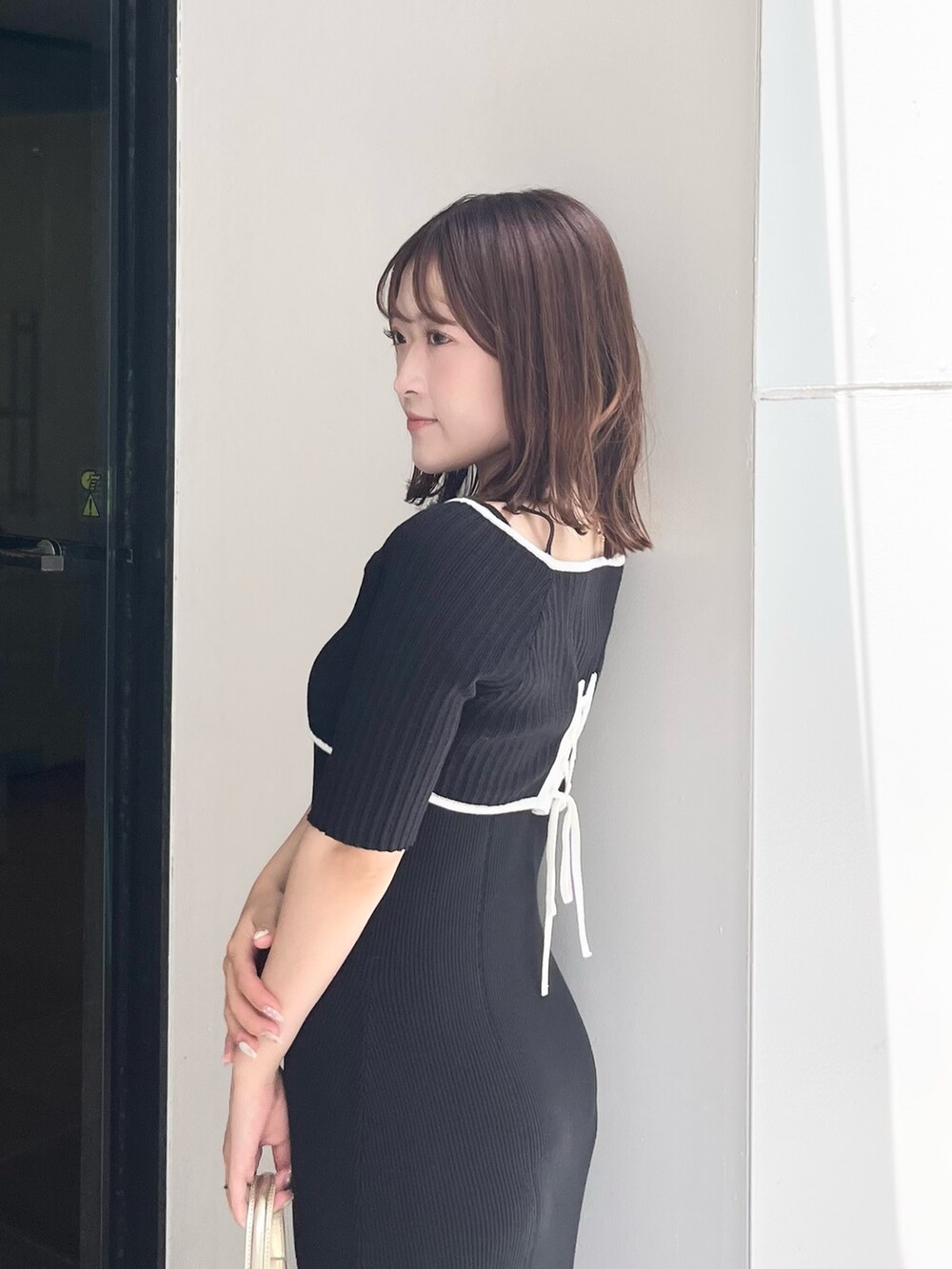 ブラック系のワンピース、ゴールド系のハンドバッグ、ホワイト系のブーツを着用したレディースの夏コーディネートの5枚目の写真