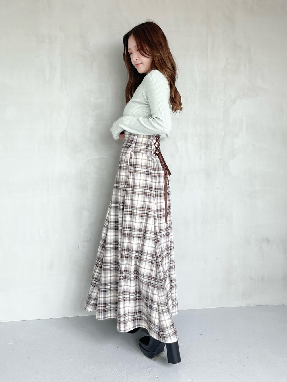 ブラウン系のスカート、グリーン系のニット/セーター、ブラック系のブーツを着用したレディースの秋コーディネートの2枚目の写真