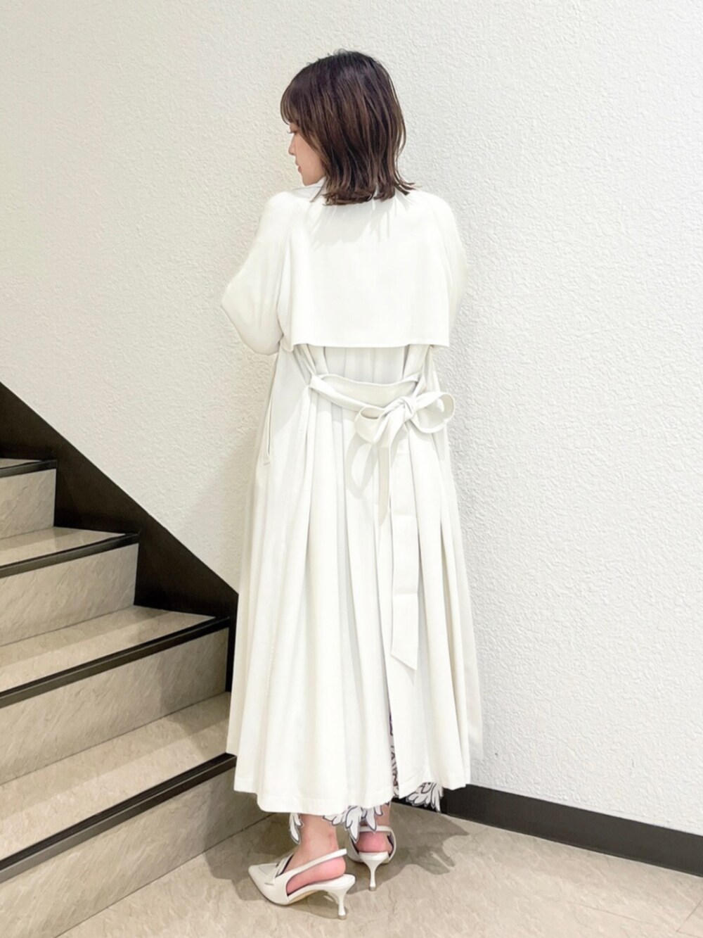 イエロー系のトレンチコート、ホワイト系のニット/セーター、ホワイト系のスカートを着用したレディースの冬コーディネートの3枚目の写真