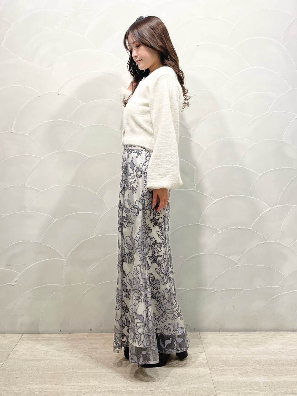 ホワイト系のカーディガン/ボレロ、グレー系のスカート、ブラック系のブーツを着用したレディースの冬コーディネートの2枚目の写真